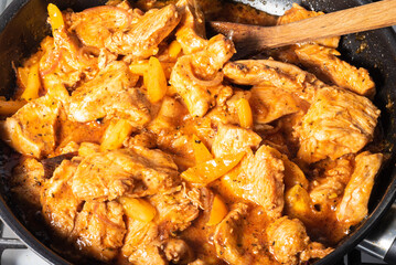 Indian style chicken cooking. Cooking traditional chicken curry. Chicken pieces are cooked in a pan and spicy curry sauce and mixed with a wooden spoon, close-up.