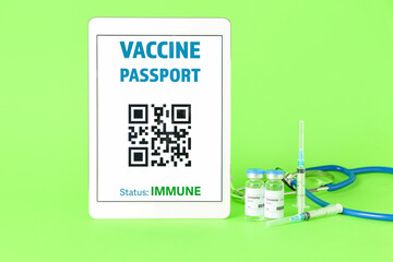 Electronic immune passport on screen of tablet computer and covid-19 vaccine on color background