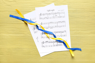 Sheet music with ribbons in colors of Ukrainian flag on yellow wooden background