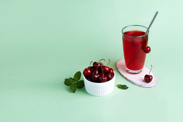 Cherry compote in a glass, berries in transparent bowl on a green background. 