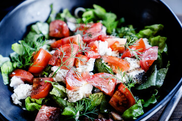 Salad with goat cheese, tomato, iceberg lettuce in big black bowl. Healthy eating, healthy lifestyle concept.