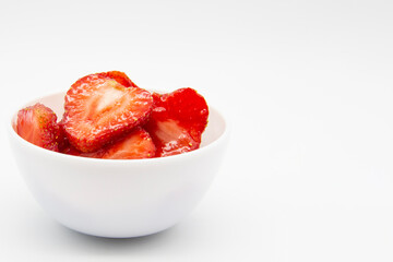 Sliced ​​strawberries in a white plate against white background. Sweet berry dessert with copy...