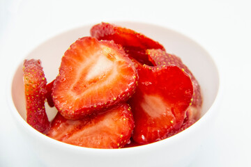 Sliced ​​strawberries in a white plate against white background.