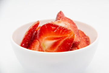 Sliced ​​strawberries in a white plate against white background.