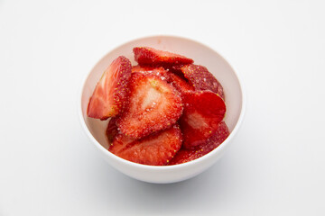 Sliced ​​strawberries in a white plate against white background.