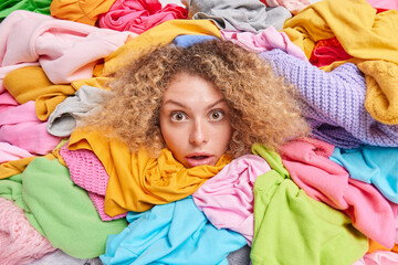 Wardrobe arrangement. Womans head sticking through pile of colorful clothes involved in old...