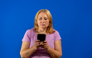 Pretty middle aged woman using her smartphone very serious isolated on blue studio background