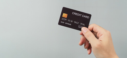 Hand is holding black credit card isolated on grey background.