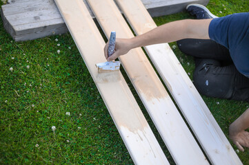 the nerdy guy is painting the wooden planks outside with cloudy weather