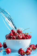 Cherries bowl with pouring water on the blue background