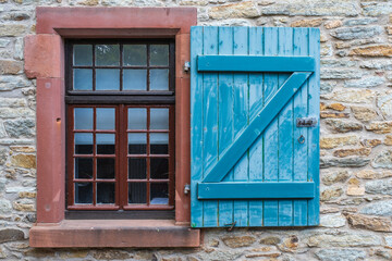 Fototapeta na wymiar View of an old stone wall with a window with a blue shutter 