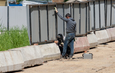 The welder welds the fence and the locksmith helps him