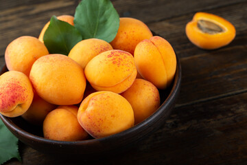 Ripe apricots and apricot leaves in a bowl on a wooden table. Fresh fruits from the home garden.