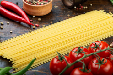 Raw pasta with fresh tomatoes, peppers, asparagus beans, spices and cheese on a wooden table.