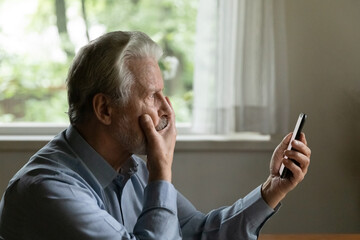 Unhappy stunned old Caucasian man look at smartphone screen shocked by bad unexpected news online....