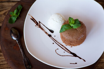 A cupcake or pancake with chocolate filling lies on a plate of ice cream. The dish is decorated for serving