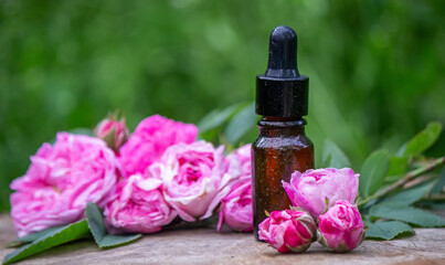 Close-up of rose essential oil bottle with falling leaves on wooden background.
