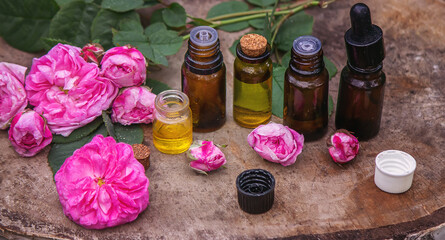 Close-up of rose essential oil bottle with falling leaves on wooden background.