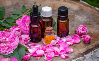 Close-up of rose essential oil bottle with falling leaves on wooden background.