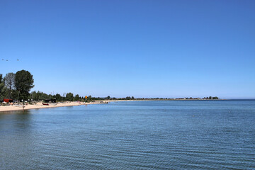 The Baltic Sea, the coast and the beach in Mechelinki in Poland. The Baltic Sea in summer. Blue sky, gulls floating on the water. People are sunbathing on the beach 