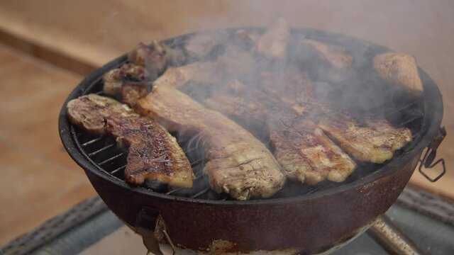 Parrillada de carne de cerdo  en la barbacoa port&aacute;til de panceta y morro, mano volteando la carne para que se ase por las dos caras