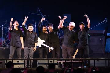 Asian group of musician men rock band standing together on stage raising fist and smiling to...