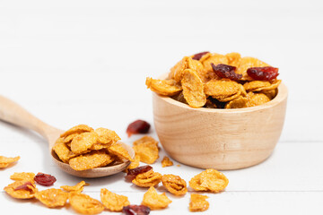 The wooden bowl of caramel cornflakes with raisins on white background for healthy eating and breakfast concept