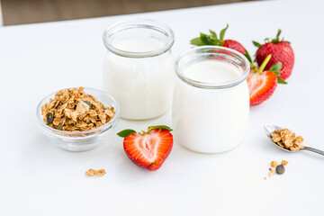 Greek yogurt in a glass jar with muesli and strawberries at the white table.