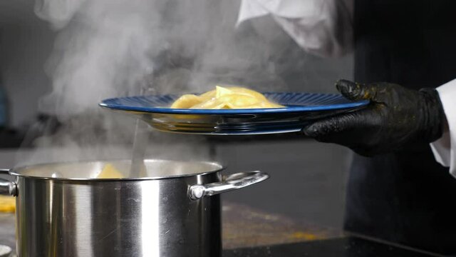Serving ravioli pouring sauce on dish. Cooking in restaurant kitchen. Freshly cooked Italian dish. steaming pan on oven. Professional chef at restaurant kitchen serves dish adding final ingredient. 4