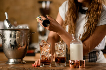 close-up of transparent glass with ice into which woman pours liquid from jigger