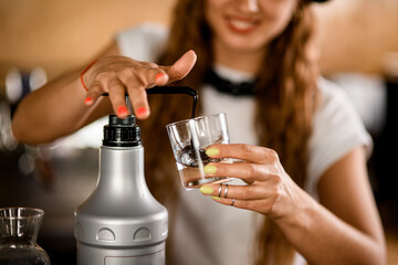 woman's hand pressing on dispenser while squeezing delicious topping into transparent glass
