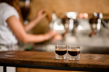 view of two transparent glasses of freshly brewed espresso on wooden table