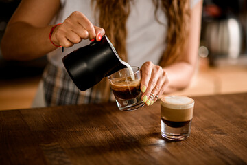view of glass with coffee drink in which woman barista pours whipped milk cream