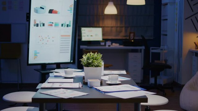 Modern empty business corporate office meeting room is ready for businesspeople late at night. In background on conference table standing company financial documents with economy graphs