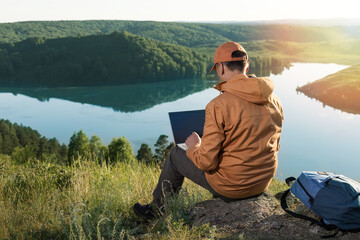 Remote work concept. Man sitting alone in nature wilderness working on laptop.