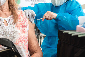 Closeup of an old Filipino woman receiving a dose of COVID-19 vaccine from a healthcare worker....