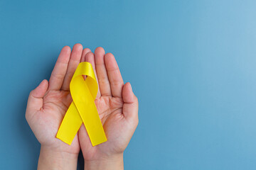 Two hands holding yellow ribbon, symbol of cancer awareness, medical support and prevention with helping hand. Suicide prevention day concept