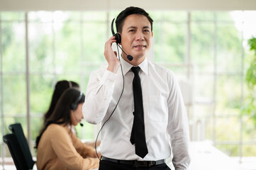 Team of call center staff in Asia wears headphones with a microphone. Smile while serving customers at desks and computers. Service concept and consulting. Communication concept.