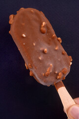 Bâtonnet glacé au chocolat tenu en main en gros plan sur fond noir