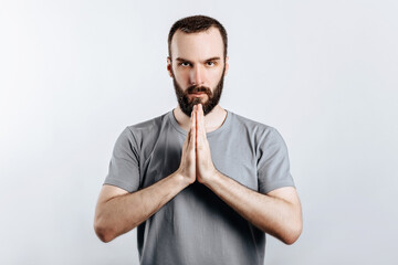 A man with crossed palms. The guy reads a prayer with his palms crossed in front of him. Portrait of handsome young man n white background with space for advertising mock up