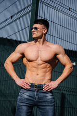 A young sexy athlete with perfect abs poses topless in jeans outside on a sunny day. Healthy...
