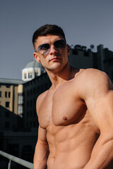 A young sexy athlete with perfect abs poses topless in jeans outside on a sunny day. Healthy...