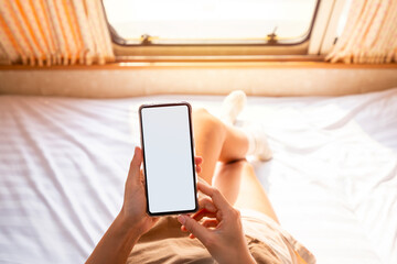 Young woman traveler laying in camper van and using smart phone while road trip traveling on vacation