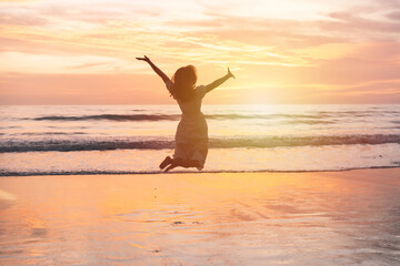 Fototapeta na wymiar Young woman jumping on the beach at beautiful sunset, Summer vacation concept