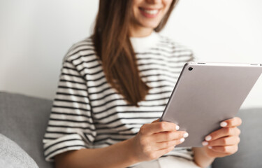 Cropped shot of smiling woman using tablet, girl reading or watching smth online on her gadget while sitting at home on sofa
