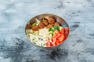 metal bowl with tomato salad, cucumbers, feta cheese, lettuce with falafel balls and chickpea hummus