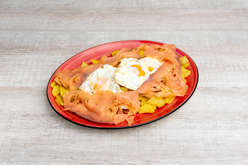 Red tray of fried eggs with smoked salmon slices on bed of chips