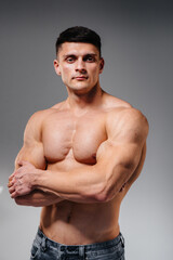 Naklejka premium A young sexy athlete with perfect abs poses in the studio topless in jeans on the background. Healthy lifestyle, proper nutrition, training programs and nutrition for weight loss.