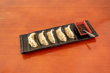 Japanese dumplings cooked on the grill with soy sauce on a black rectangular plate