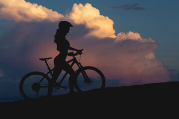 Fototapeta na wymiar Girl on a mountain bike on offroad, beautiful portrait of a cyclist at sunset, Fitness girl rides a modern carbon fiber mountain bike in sportswear.